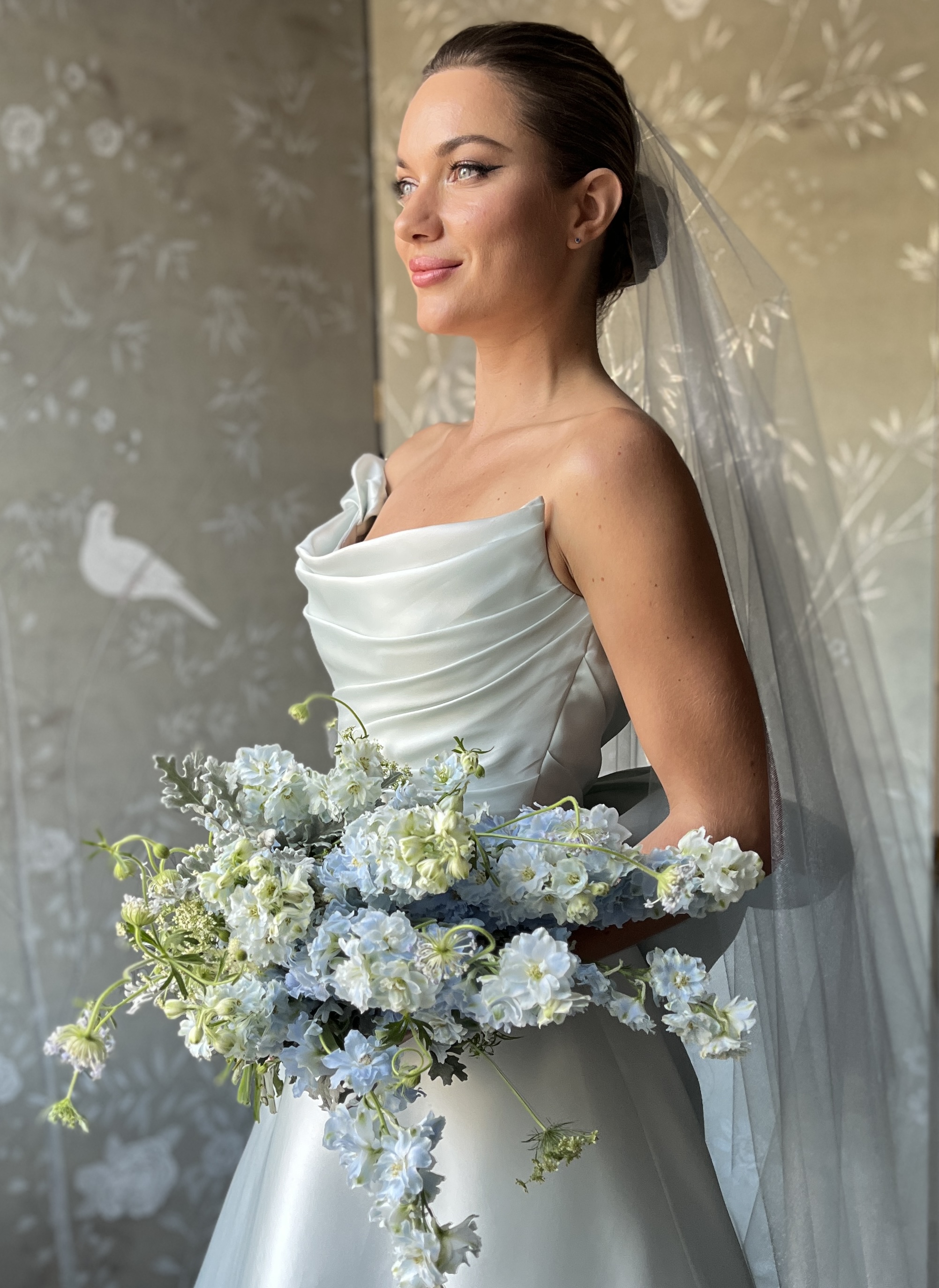 Bride in a strapless satin gown holding a pale blue and white floral bouquet
