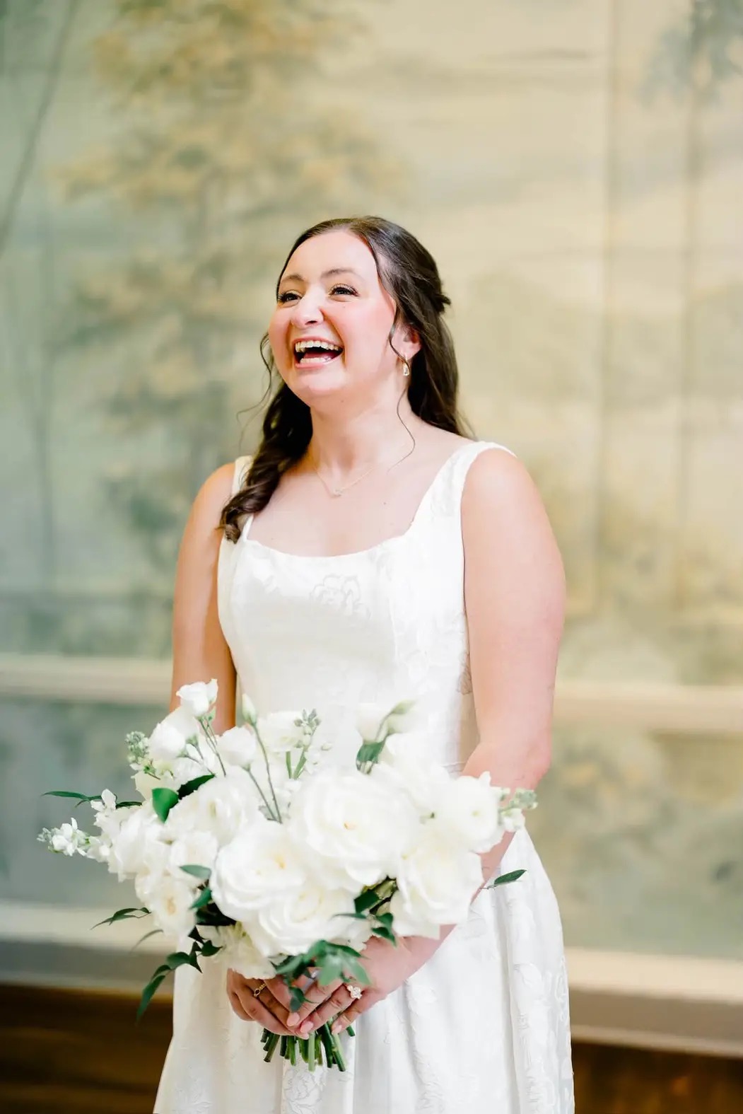 Shira laughing joyfully in her wedding gown, holding a white rose bouquet